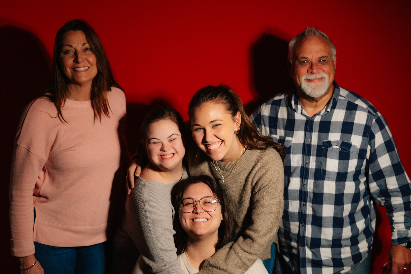 A smiling multi-generational family poses together in front of a red backdrop.